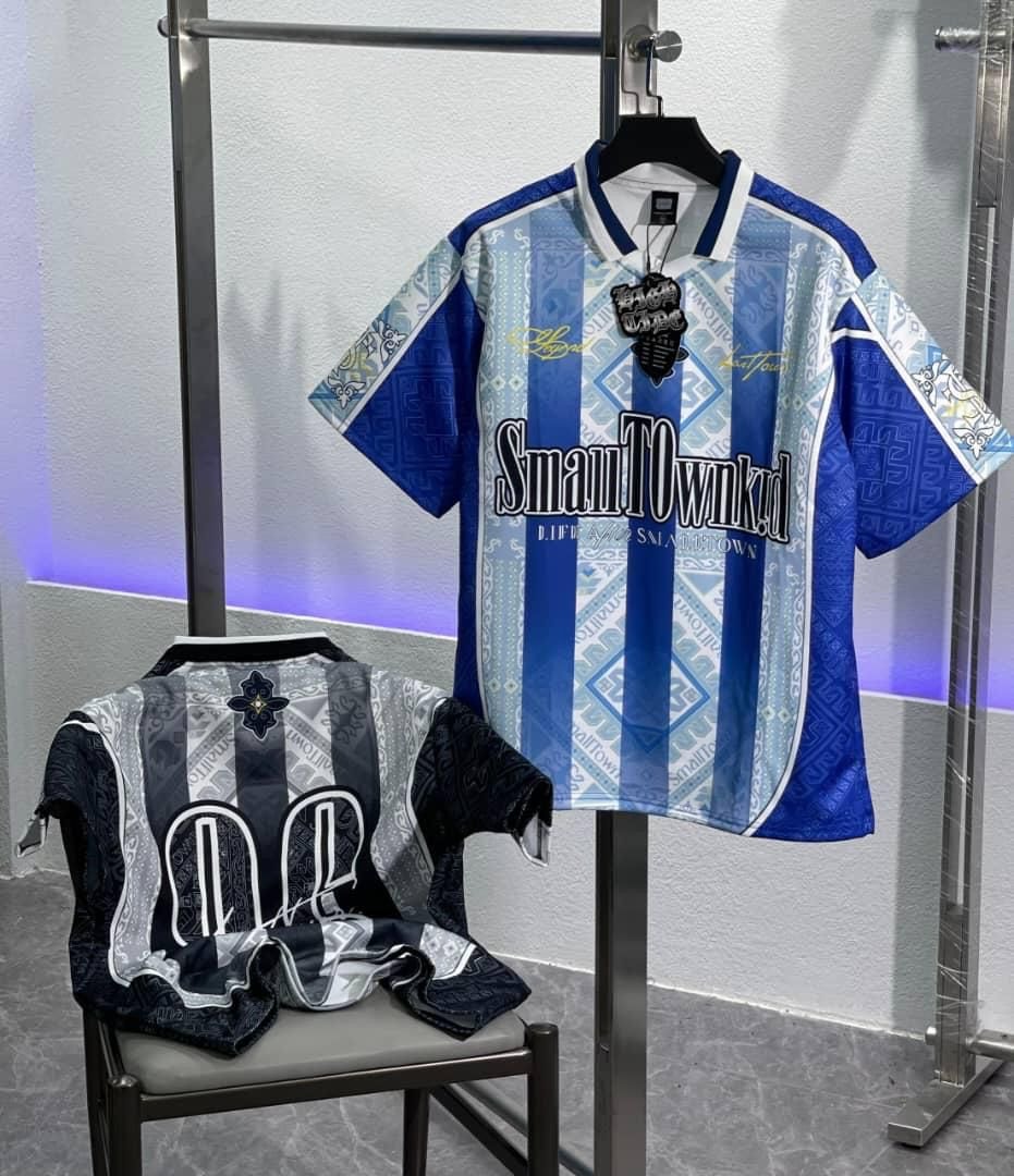 Two graphic jerseys displayed together: one in blue and white with central text, the other in black, grey and white patterned design.