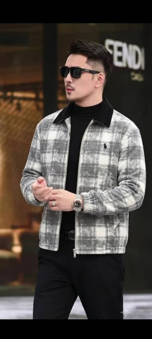 Man wearing gray and white plaid zip-up fleece jacket with black collar and chest logo over black turtleneck.