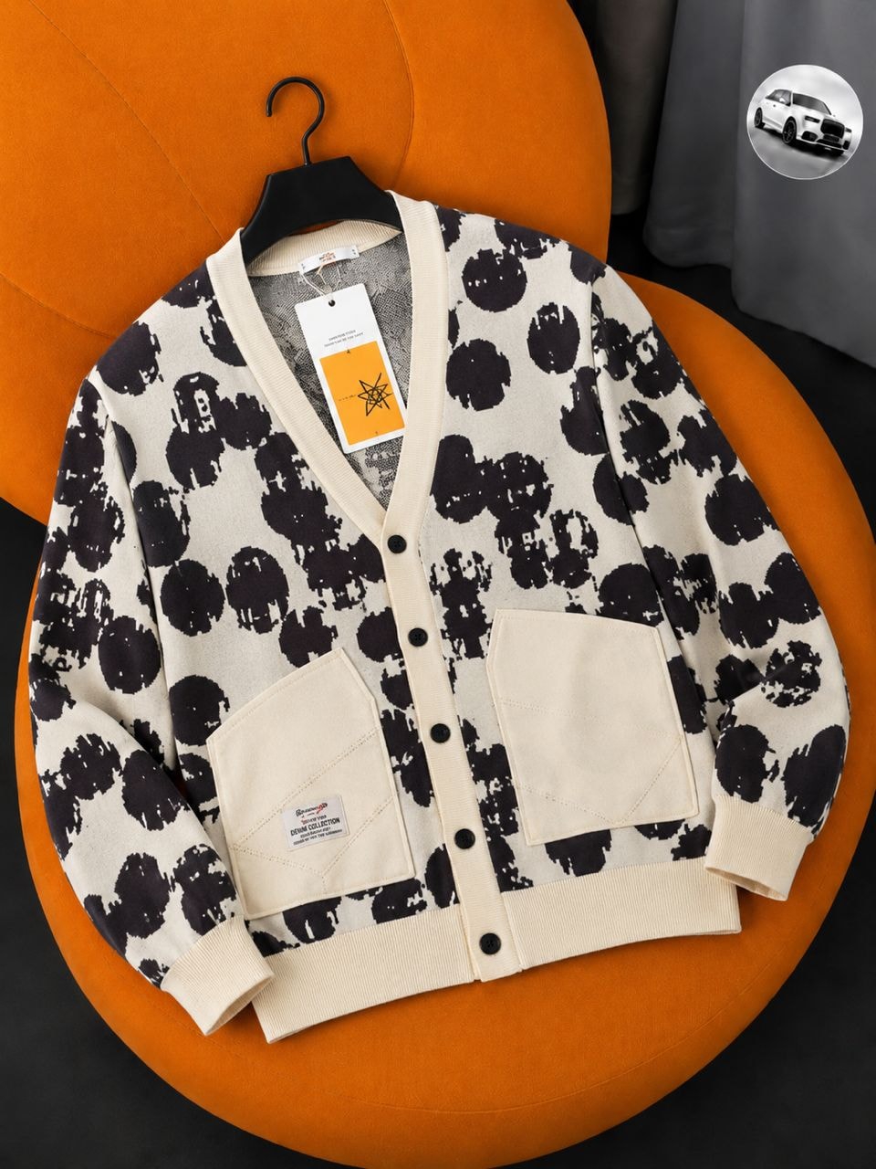 Cream cardigan with black abstract print, pockets and tags on orange chair.
