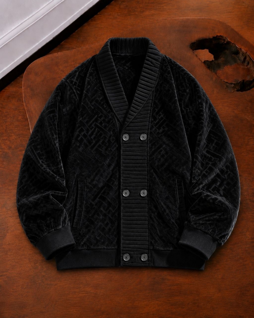 Black geometric patterned velvet bomber jacket laid flat on wooden surface.