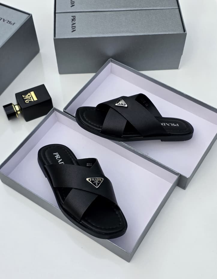 Black Prada cross-strap slides in open grey box with perfume bottle and matching packaging.
