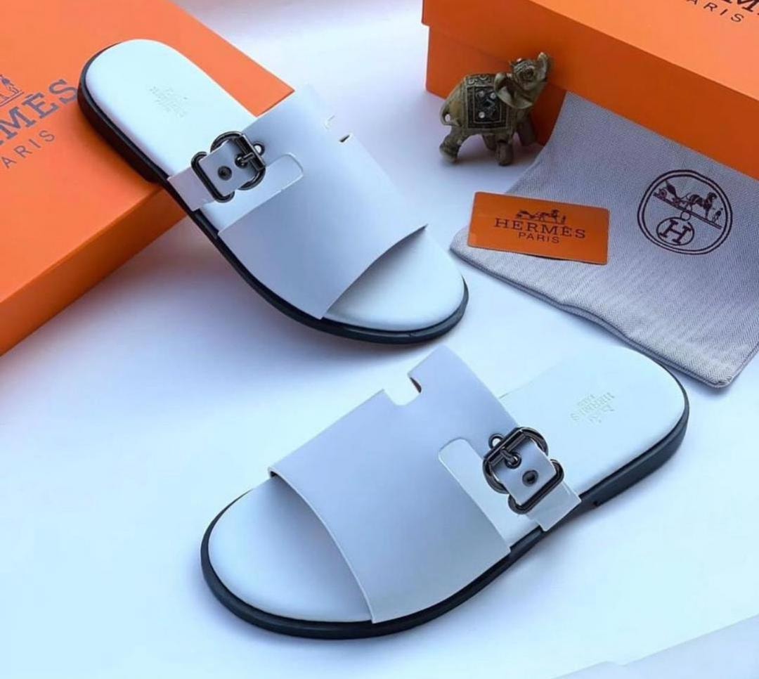 White Hermes slides with black buckle shown with orange box, dust bag and small elephant figurine.
