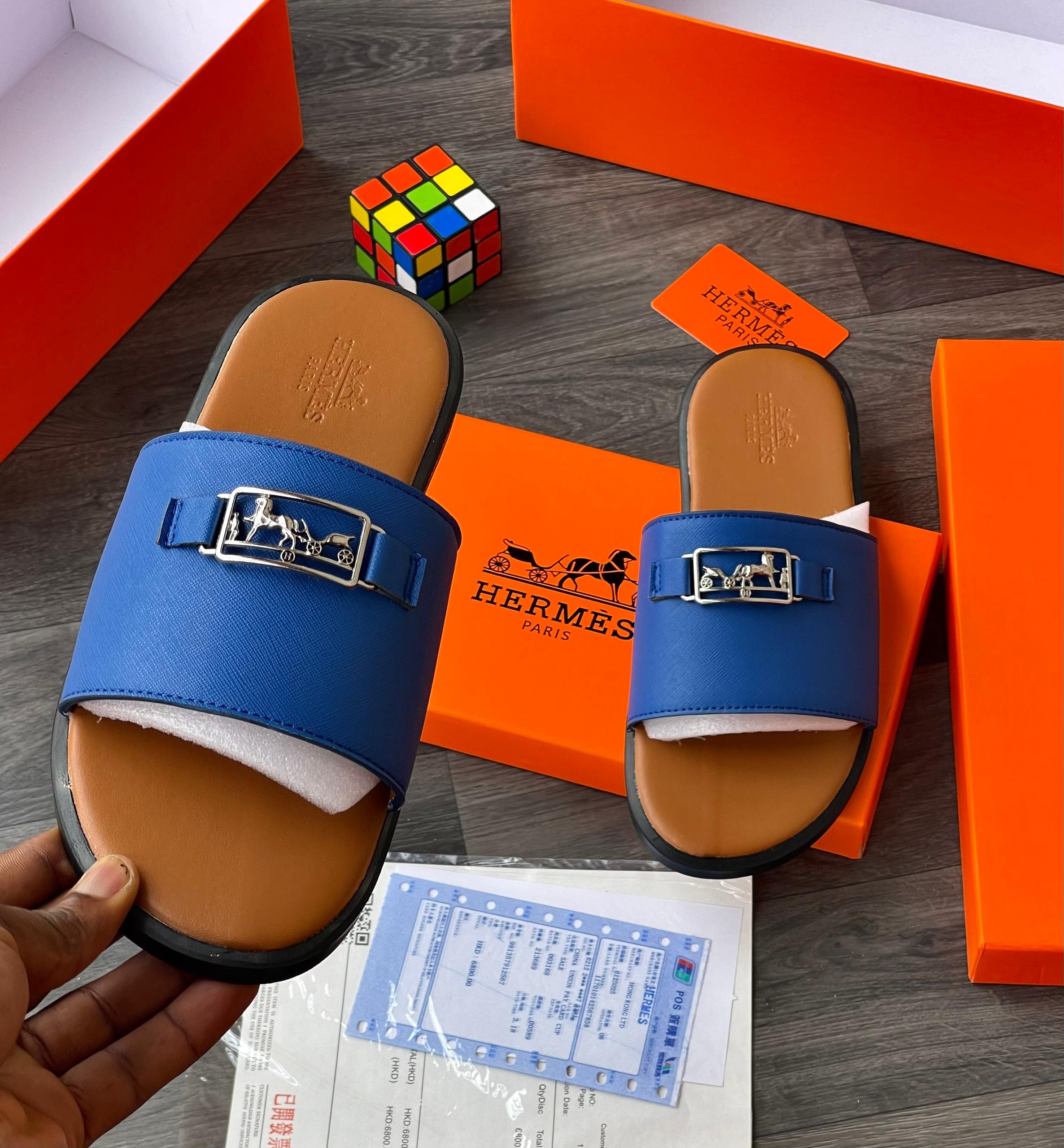 Blue Hermes slides with silver buckle displayed with orange boxes and authenticity documents.