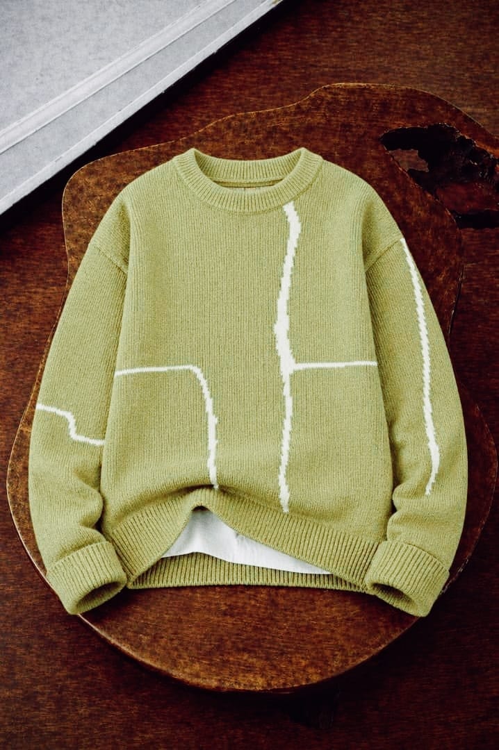 Flat lay of lime green knit sweatshirt with white abstract line designs on wooden surface.
