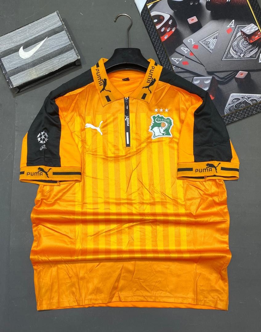 Orange and black striped Cote d'Ivoire Puma jersey laid flat on surface.