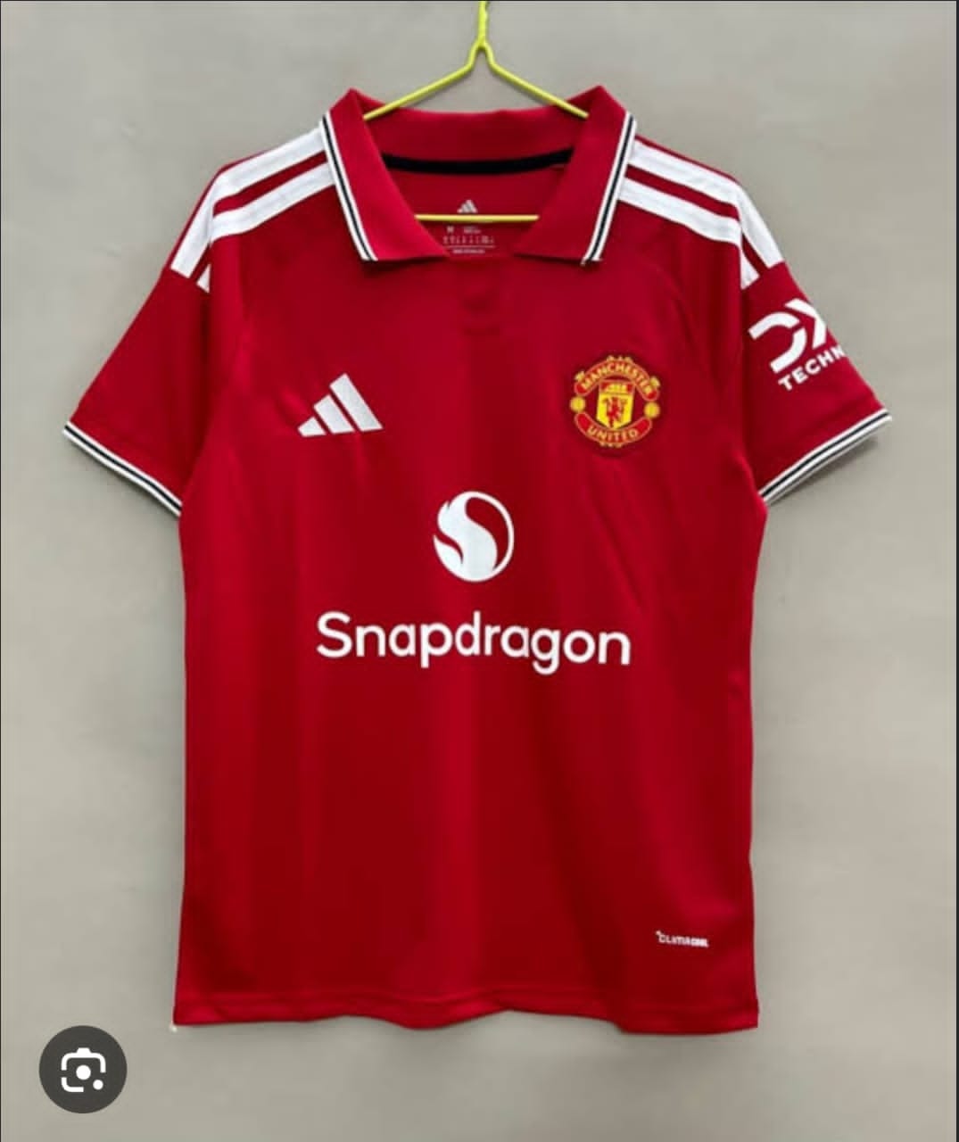 Red Manchester United adidas polo shirt hanging on yellow hanger.