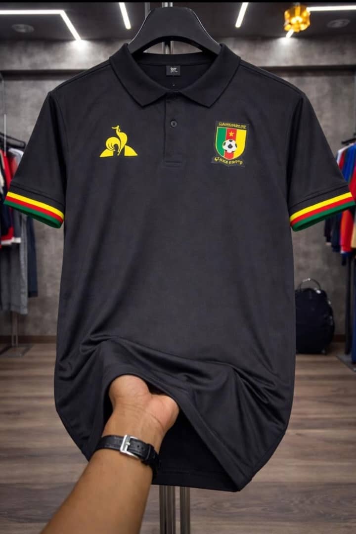 Black Cameroon polo jersey held by hand in store environment.