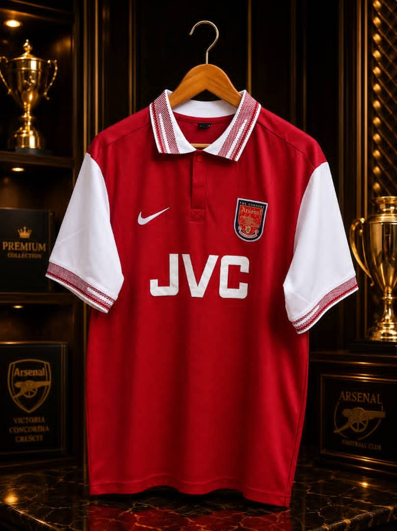 Red and white Nike Arsenal JVC jersey on wooden hanger.