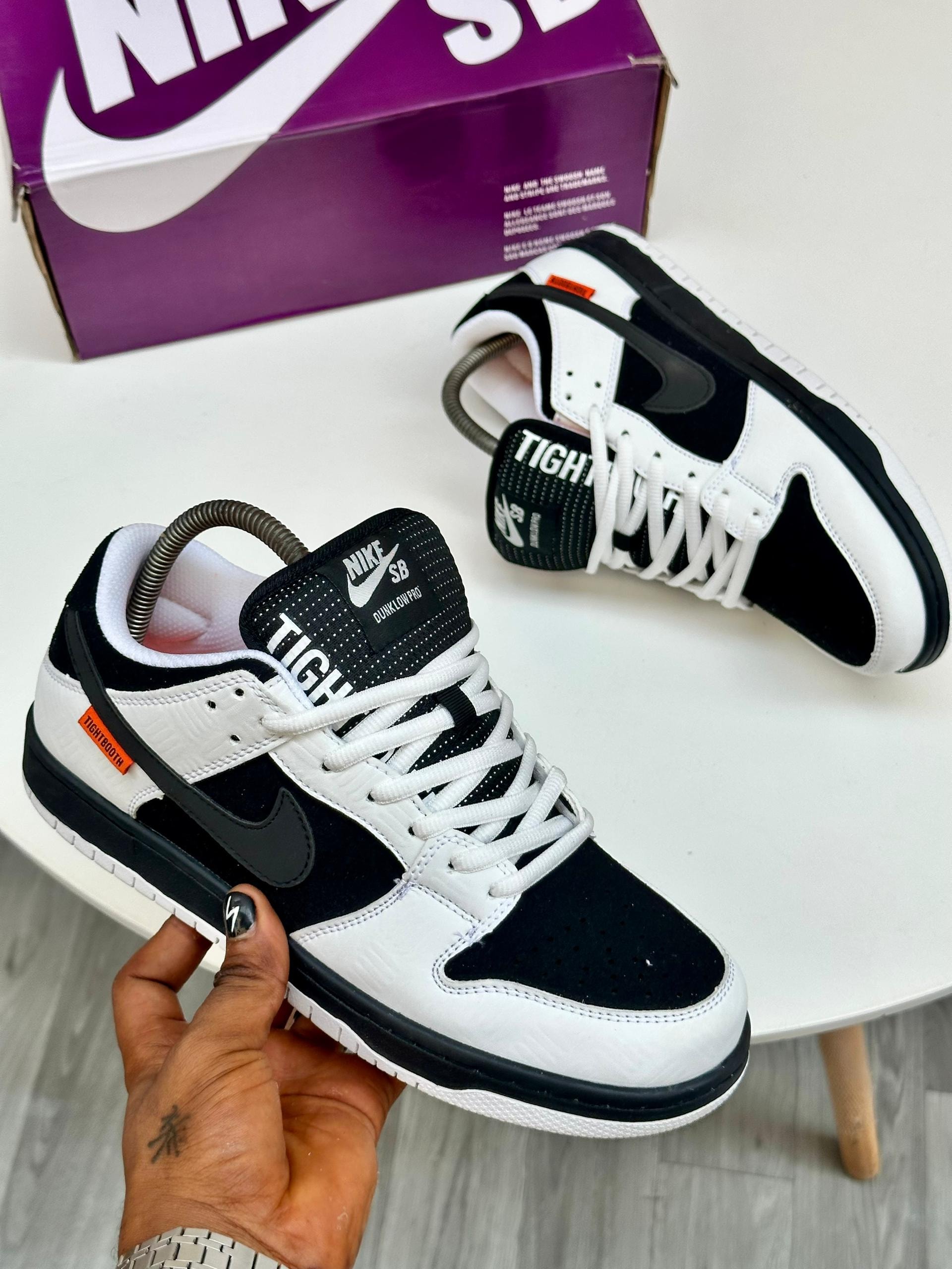 Nike SB Dunk Low sneakers in black and white held by hand and shown on table.