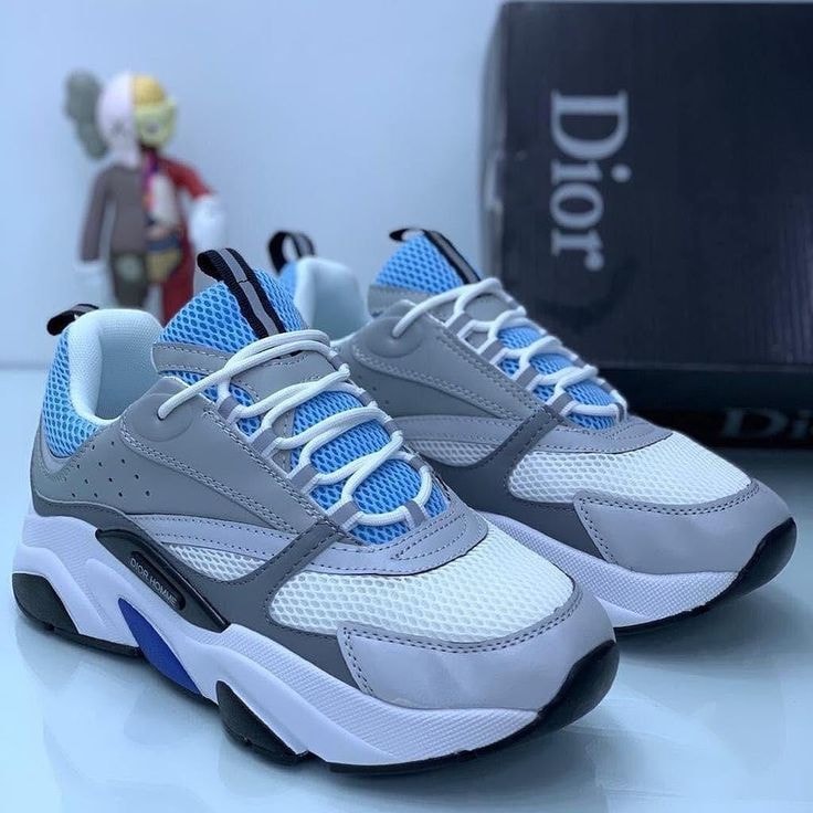 Grey white and blue Dior sneakers with mesh details and branding on a reflective surface.