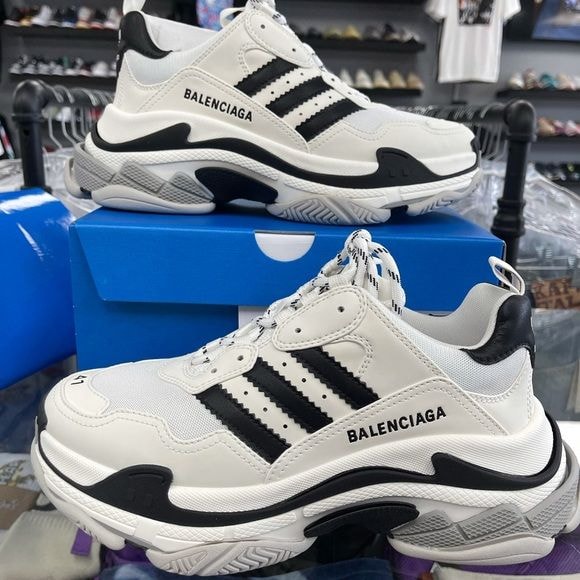 White and black Balenciaga Triple S style sneakers displayed on a blue box in a retail setting.