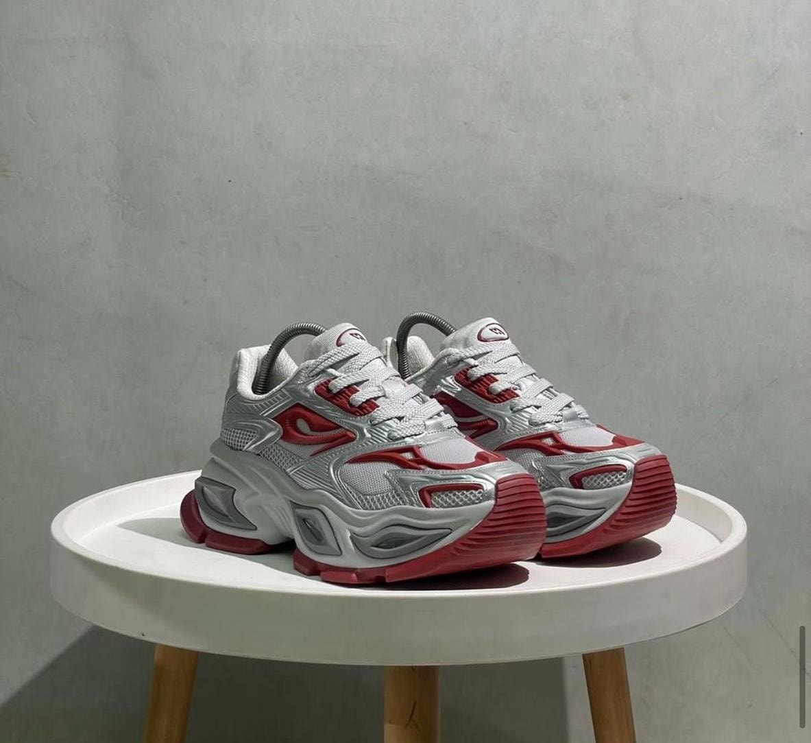 Silver, grey, and red chunky sneakers on a white table against a neutral background.