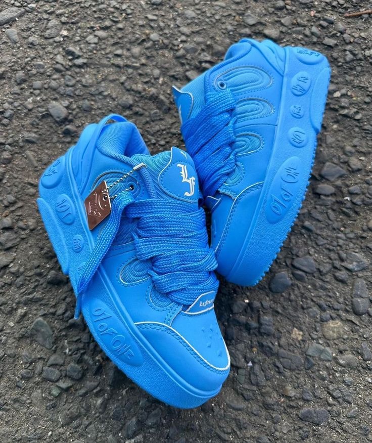 Bright blue chunky sneakers with embossed logos and thick sole on gravel ground.