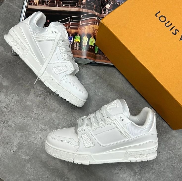 Pair of white Louis Vuitton low sneakers with orange box on grey textured surface.