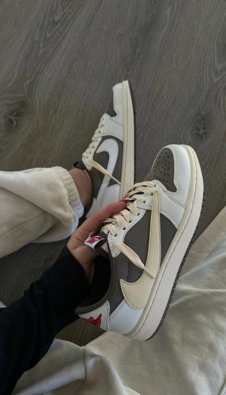 Person wearing grey white and beige Jordan 1 Low sneakers on wooden floor.