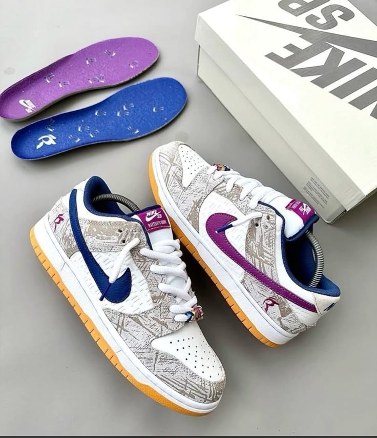 Nike Dunk Low sneakers with purple swoosh, graffiti print, insoles and shoebox on grey surface.