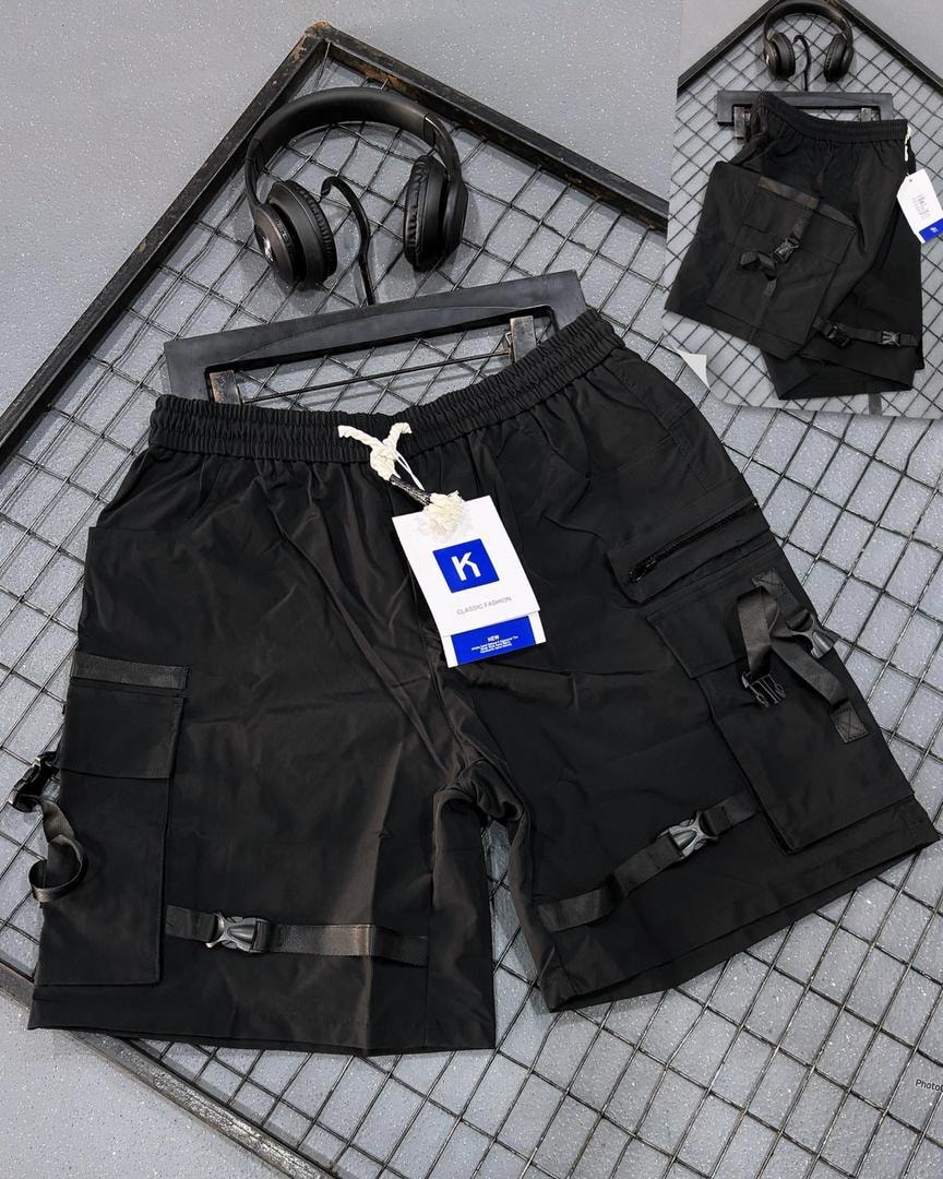 Black tactical cargo shorts with buckle straps, multiple pockets and K tag on grid background.