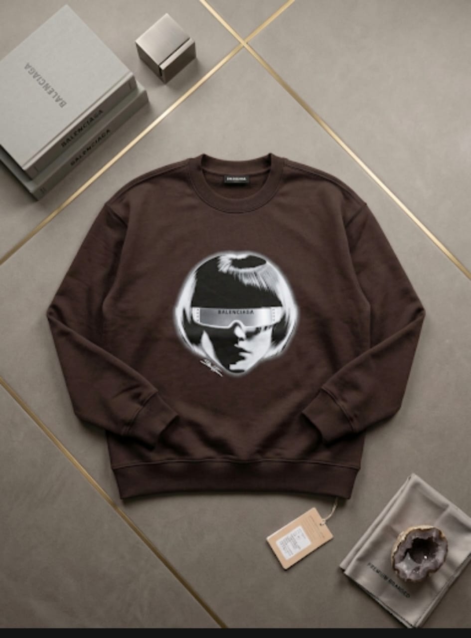 Brown crewneck sweatshirt with large circular Balenciaga visor face graphic on chest.