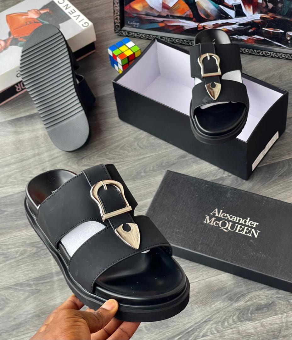 Black platform slide with gold buckle and emblem, shown with Alexander McQueen box.