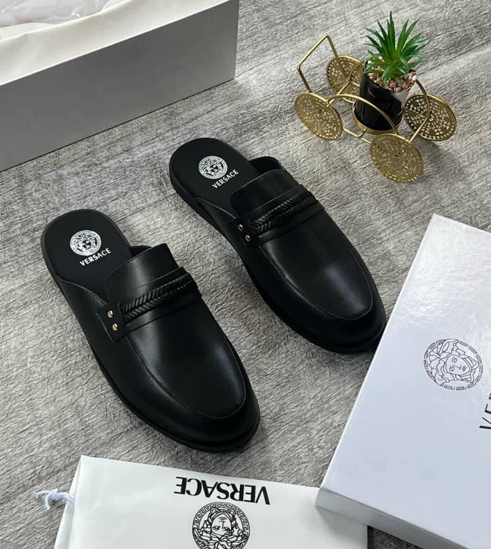 Black Versace mules with Medusa logos and rope detail, arranged with branded boxes, dust bags and plant decor.