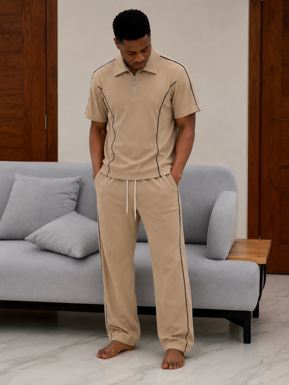Man standing barefoot in beige ribbed two-piece set with black piping details.