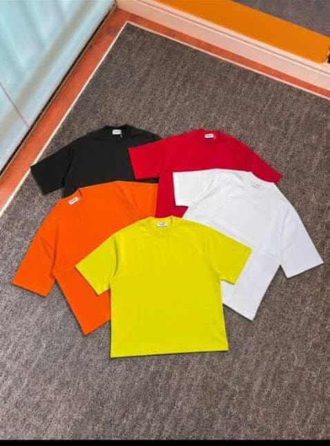 Plain crop tees in black, red, orange, yellow, and white laid out on carpet.