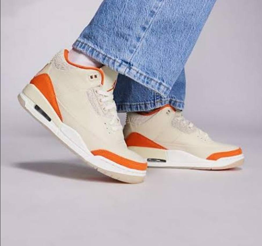 Cream and orange Air Jordan high-top sneakers worn with jeans shown from side profile.