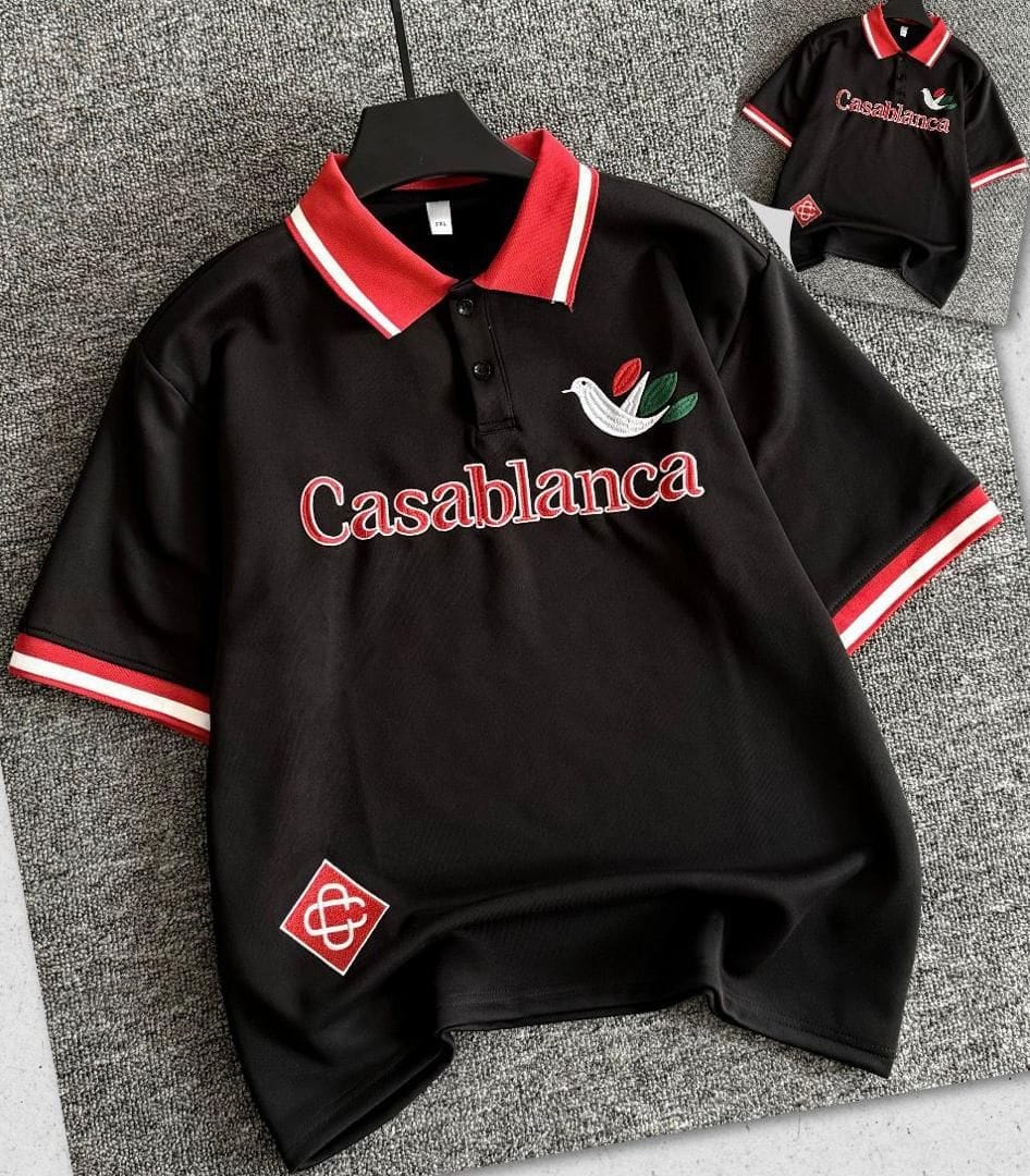Black Casablanca polo shirt with red embroidery, bird logo, and striped collar and cuffs.