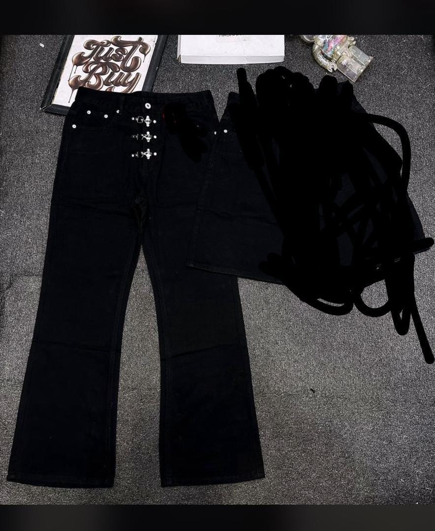 Black baggy flared jeans with ornate cross metal details on the front waist and closure, laid flat on dark surface with accessories.