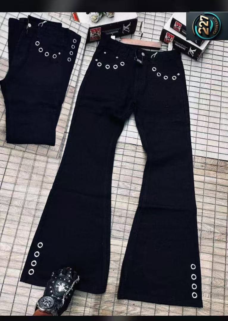 Multiple pairs of black baggy flared jeans with silver grommets on pockets and flared legs, laid flat on a tiled surface.
