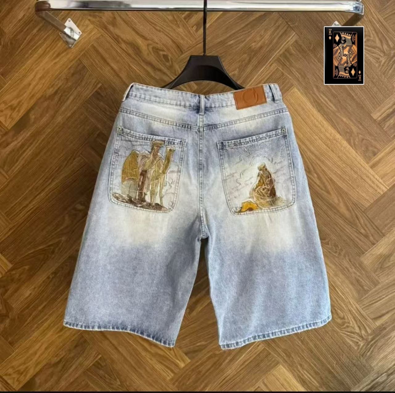 Back view of light blue denim jorts showing embroidered back pockets with camel and figure designs.