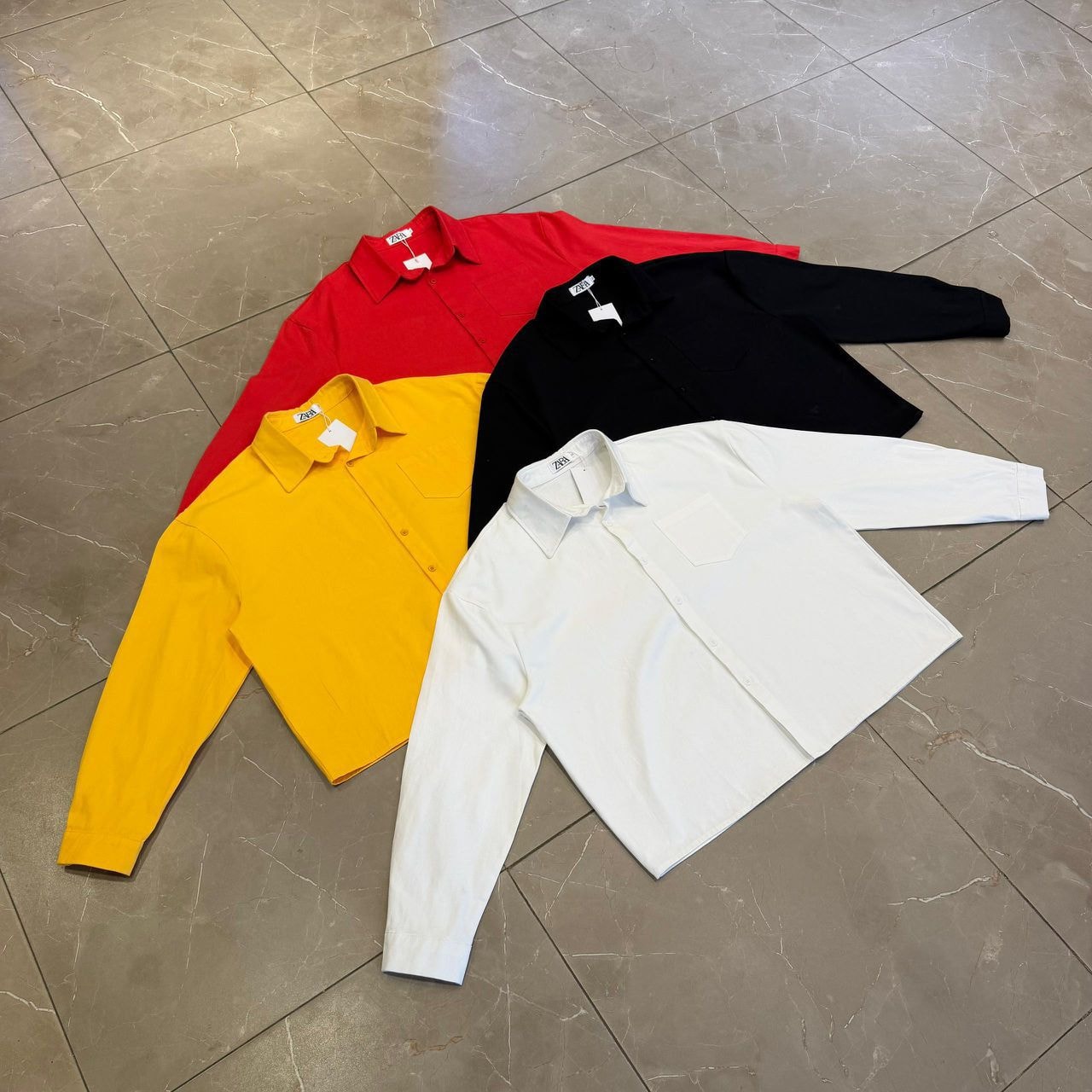 Flat lay of luxury update shirts in red, yellow, black and white on tiled floor.