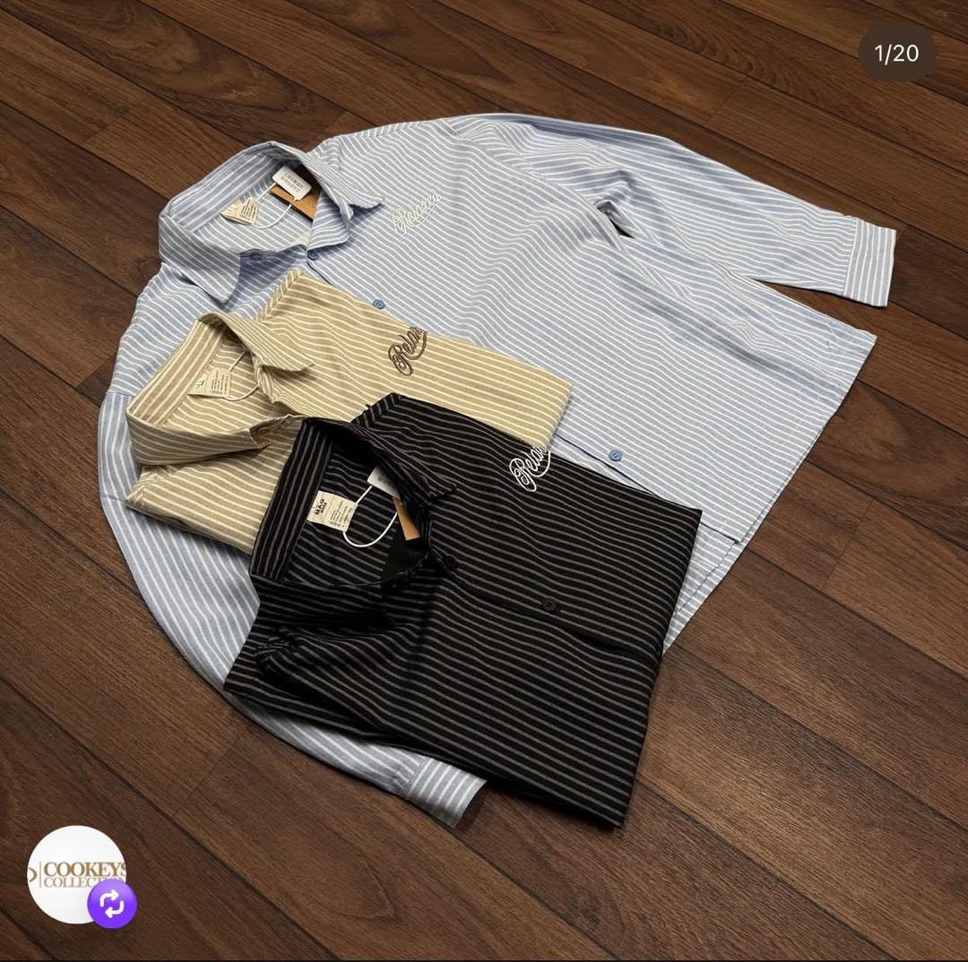 Flat lay of multiple striped button-down shirts in light blue, beige, and black on wooden floor.