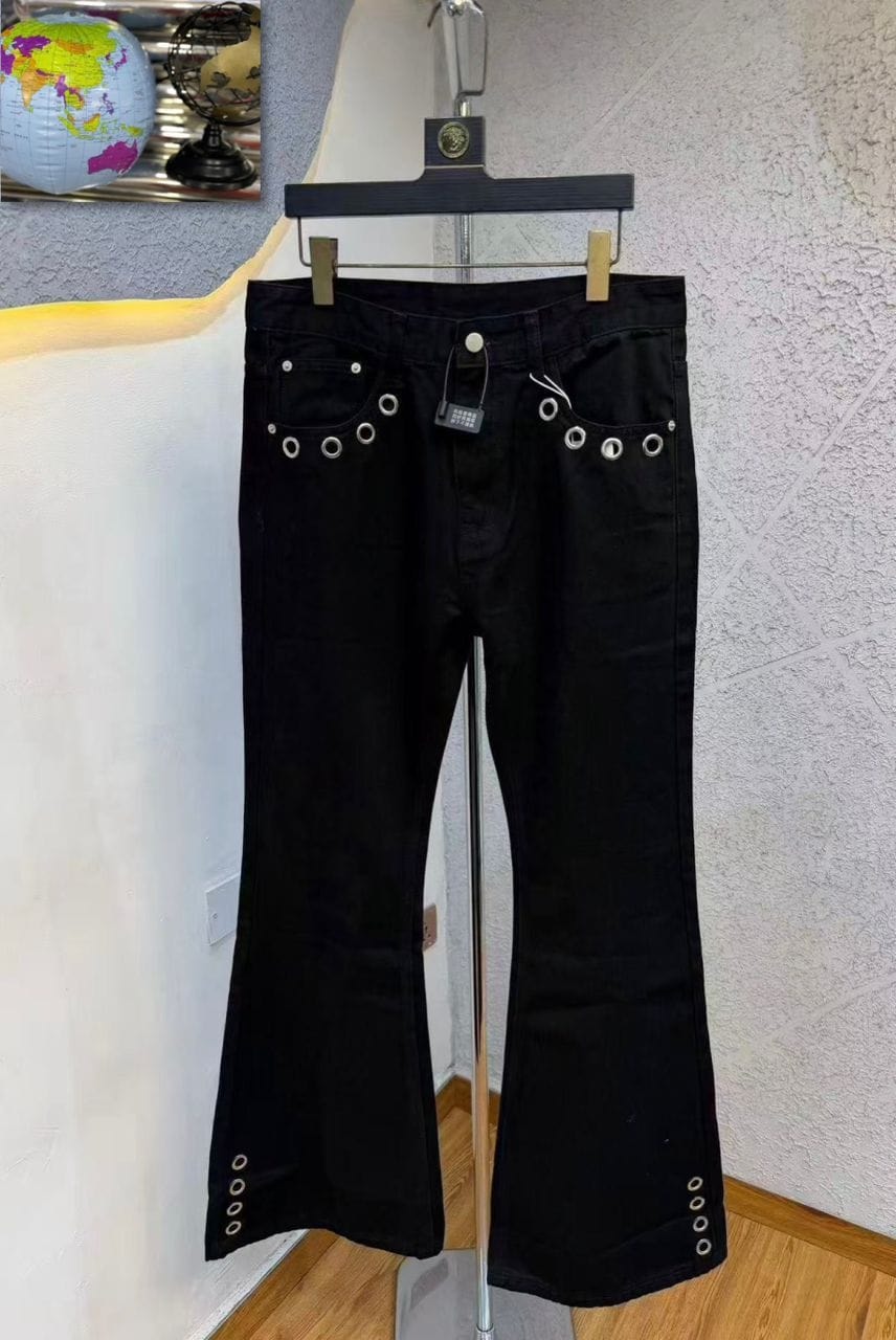 Front view of black flared jeans on hanger highlighting silver eyelets on pockets and hem.