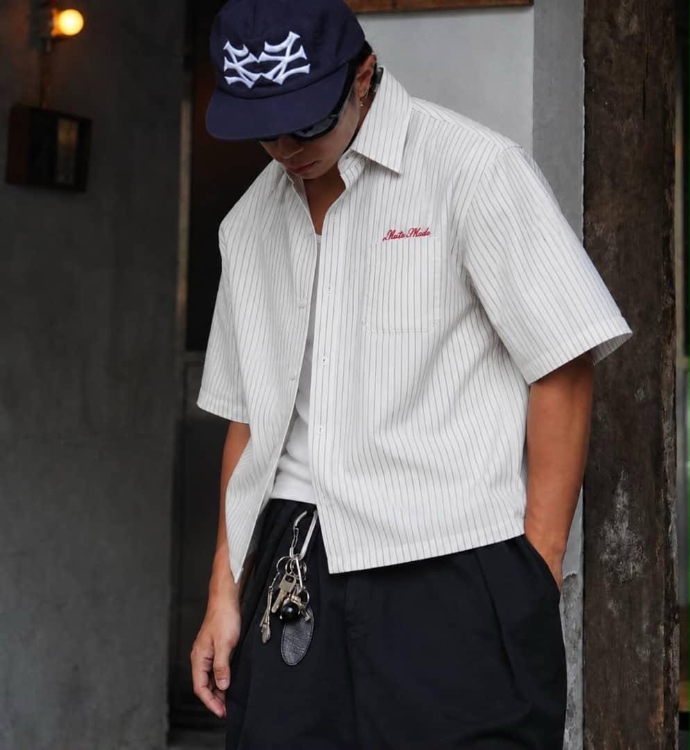 Model wearing white pinstriped short sleeve button-up shirt with red chest embroidery.