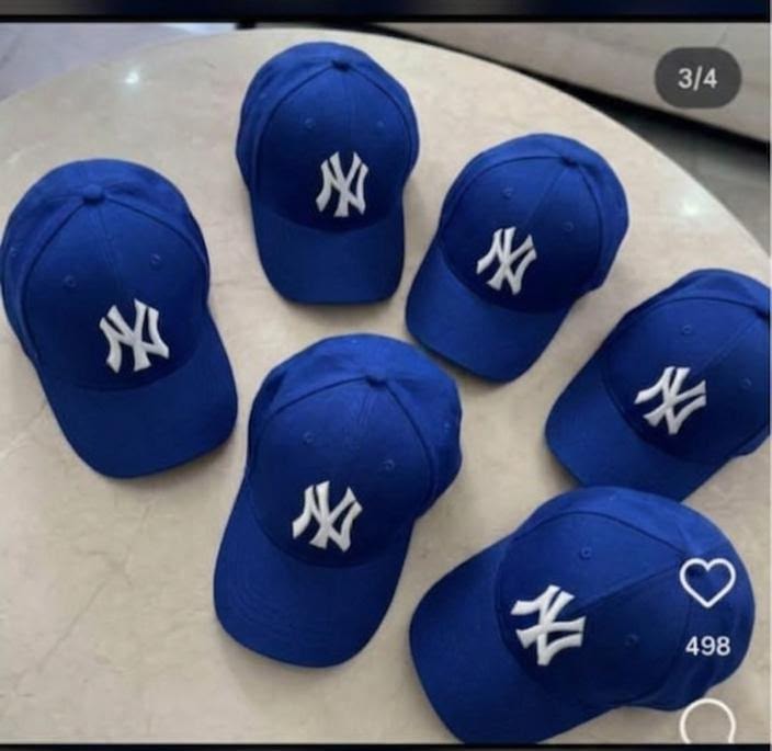 Six blue NY logo baseball caps arranged on a round table.