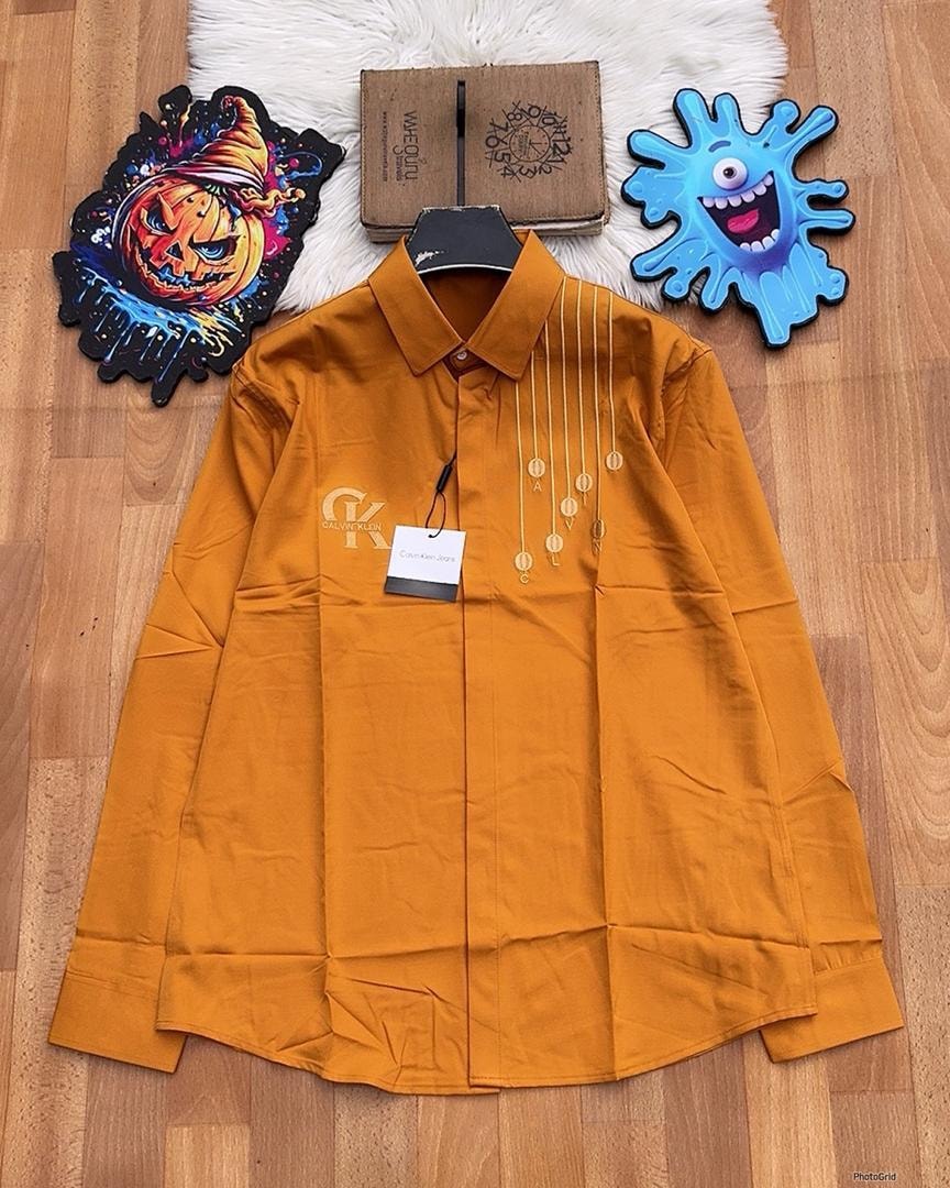 Orange Calvin Klein embroidered long sleeve button-down shirt laid flat on wooden floor.