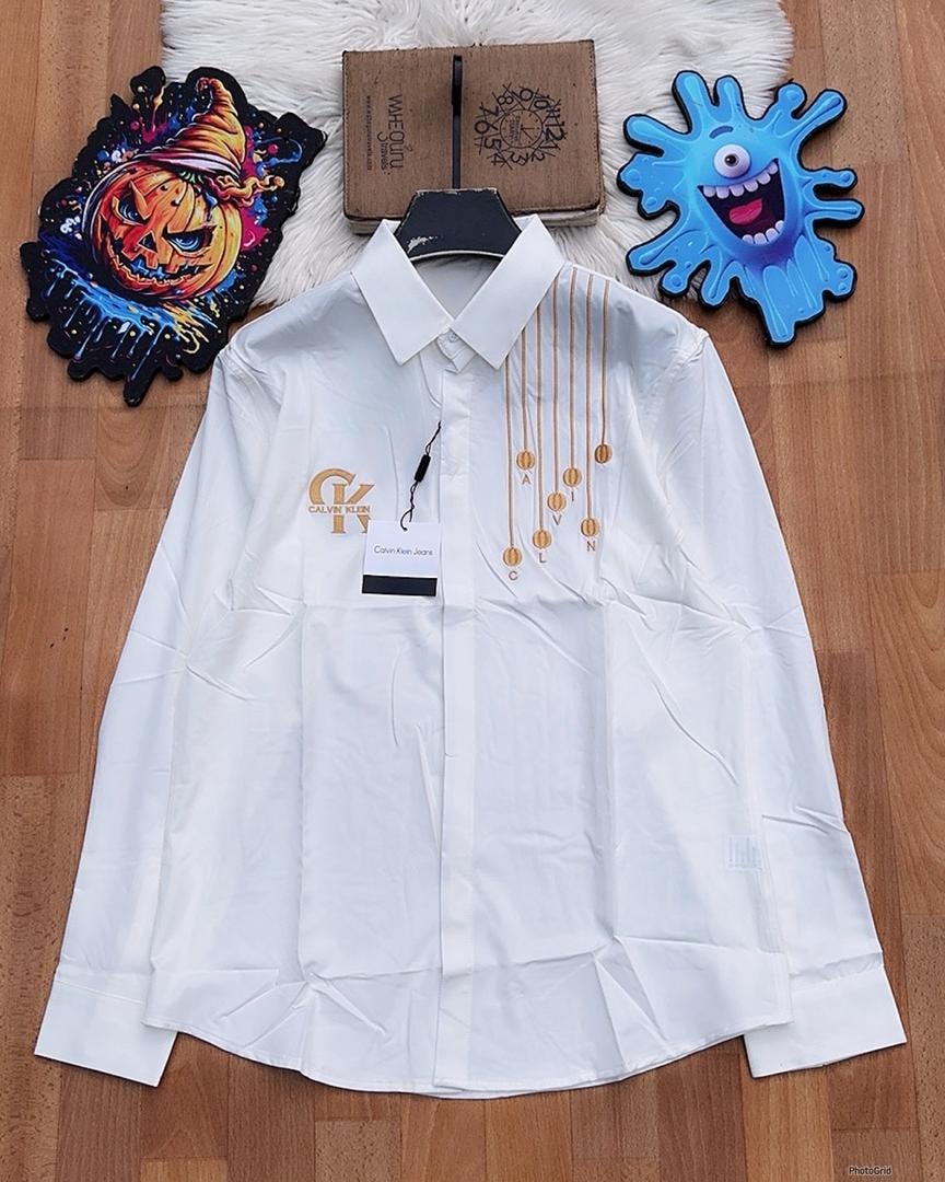 White Calvin Klein embroidered long sleeve button-down shirt laid flat on wooden floor.