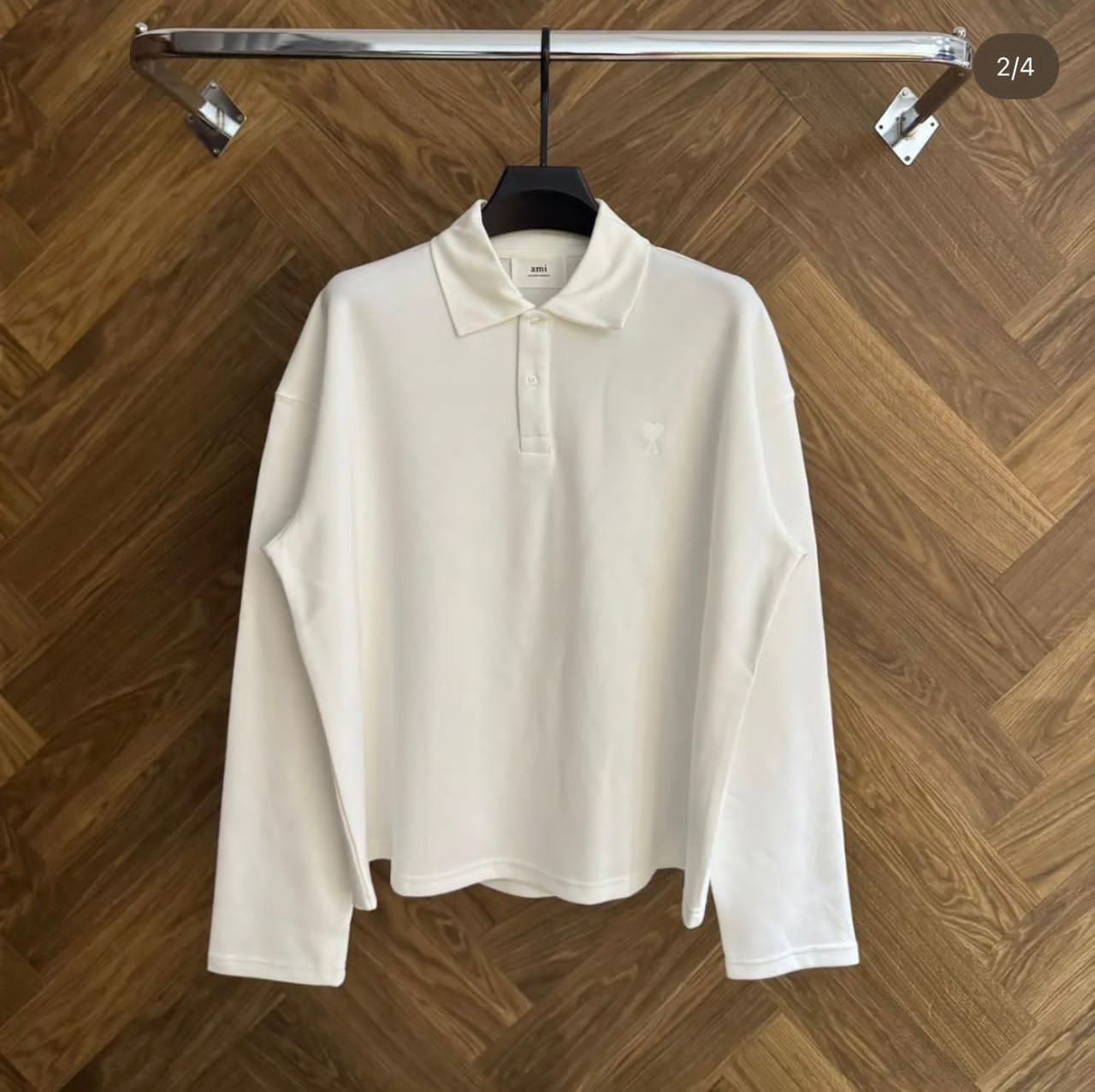 White AMI long sleeve polo shirt displayed on hanger against wooden background.