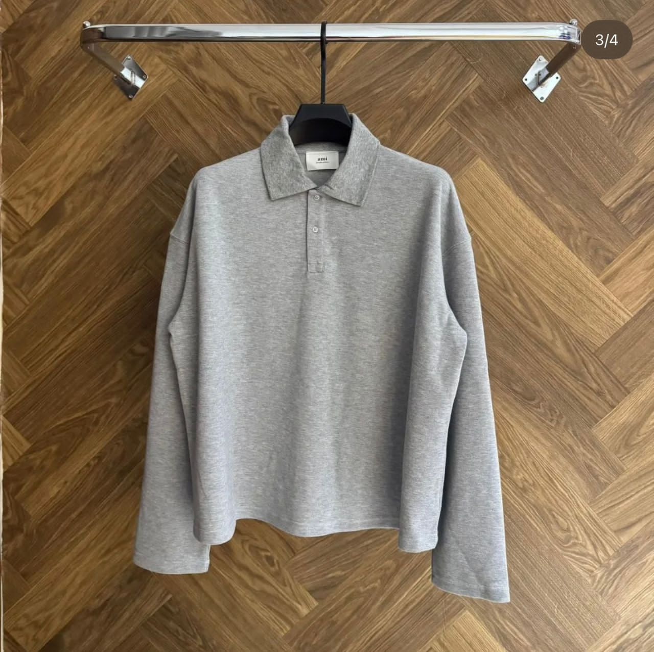 Gray AMI long sleeve polo shirt hanging on a chrome rack against wooden floor.