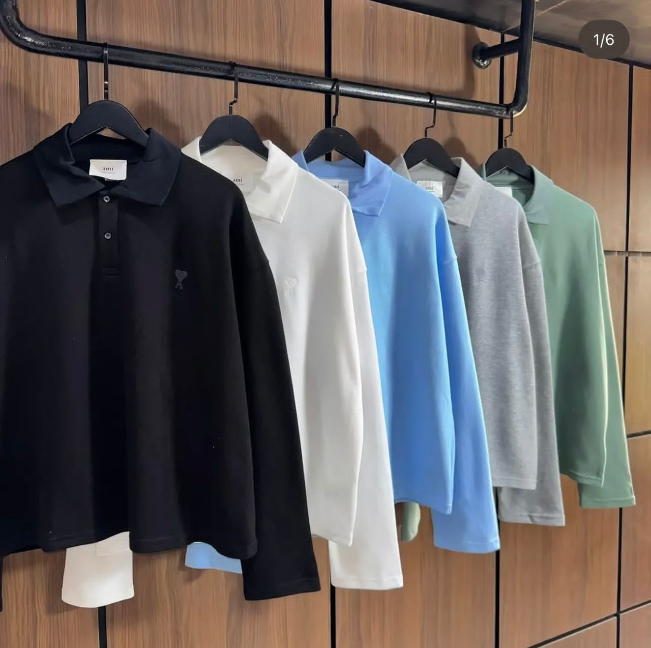 Multiple AMI long sleeve polo shirts in various colors hanging on a black rack against wood paneling.