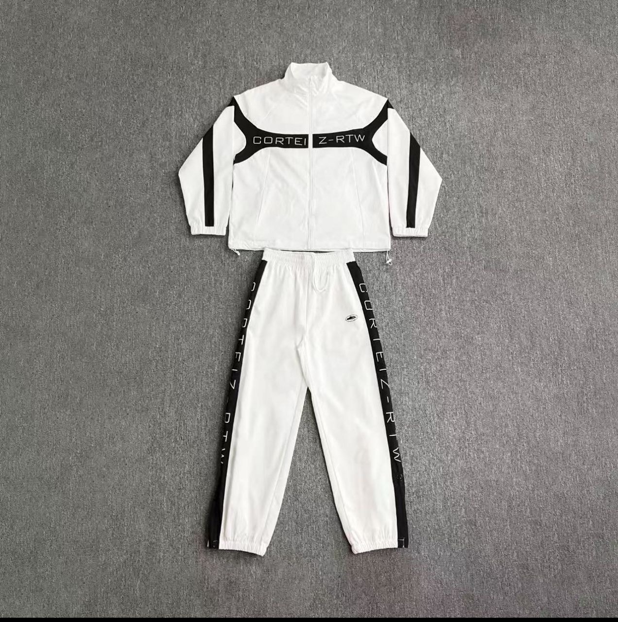 White and black Corteiz Z-RTW tracksuit set with zip jacket and jogger pants laid flat.