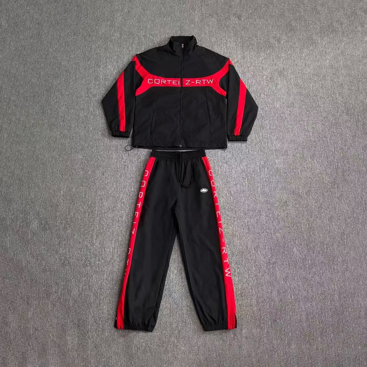 Black and red Corteiz Z-RTW tracksuit set with zip jacket and jogger pants laid flat.