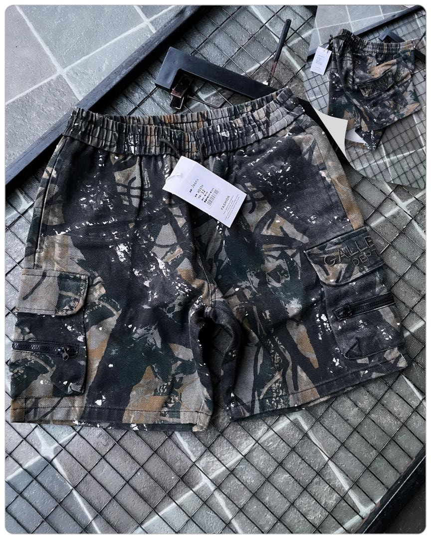 Flat lay of dark splatter cargo shorts with white tag and accessories.
