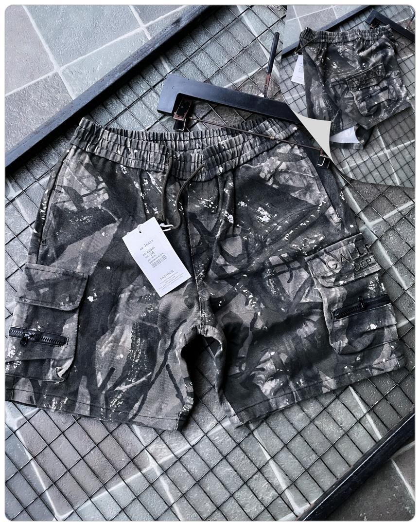 Flat lay of black splatter camo cargo shorts with tag on grid surface.