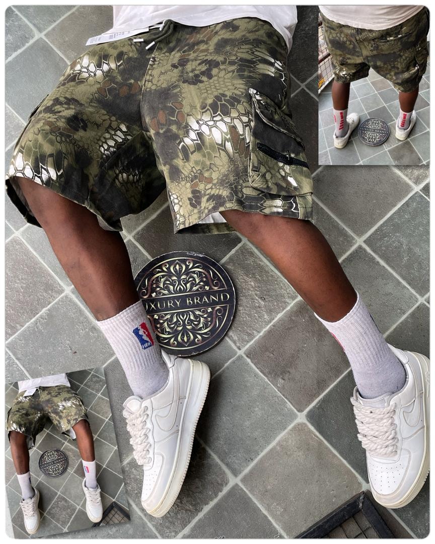 Person modeling olive green reptile camo cargo shorts with white sneakers and socks.