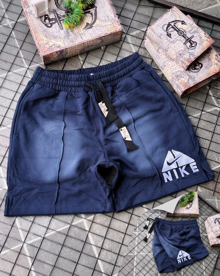 Navy Nike fleece shorts with faded gradient and embroidered logo, shown with miniature pair on tiled surface.