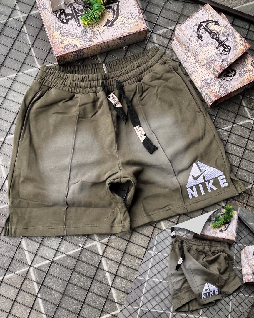 Olive Nike fleece shorts with faded gradient and embroidered logo, shown with miniature pair on tiled surface.
