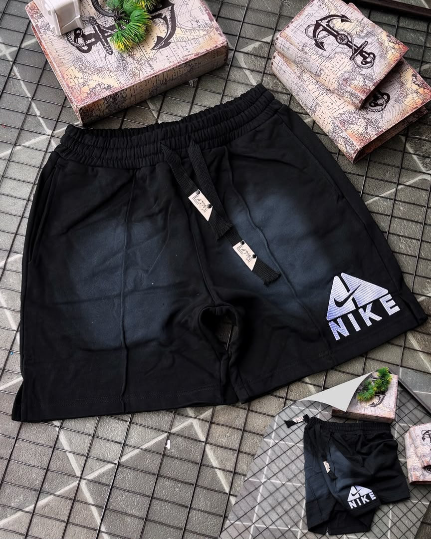 Black Nike fleece shorts with faded gradient and embroidered logo, shown with miniature pair on tiled surface.