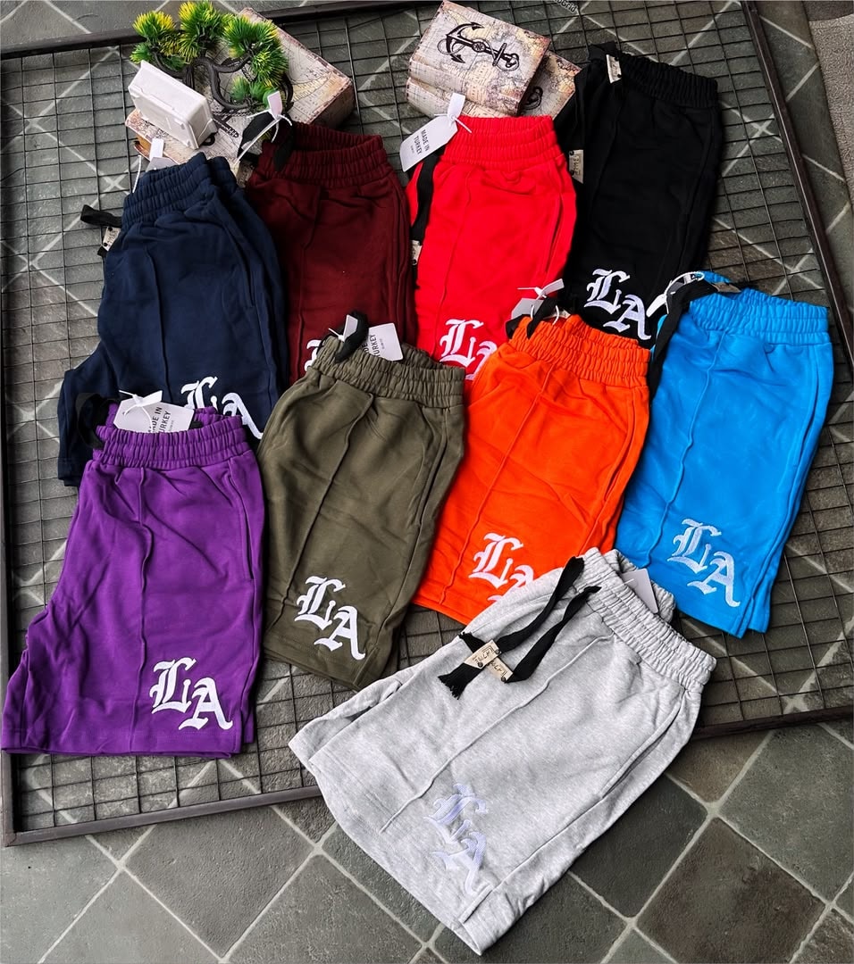 Assortment of LA embroidered fleece shorts in 9 colors on grid surface with decorative boxes.